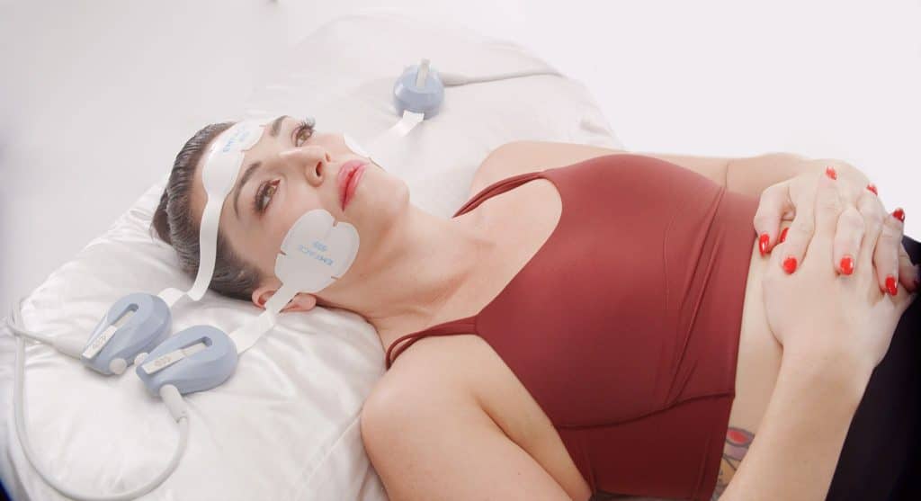 Patient lying down during an EMFACE treatment with applicators on the face.